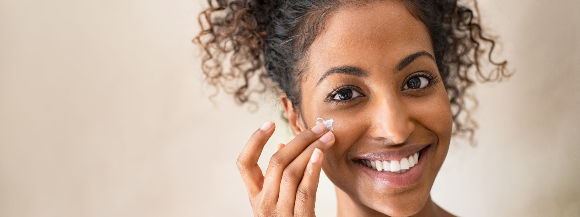 Woman applying cream to her face with a neutral background