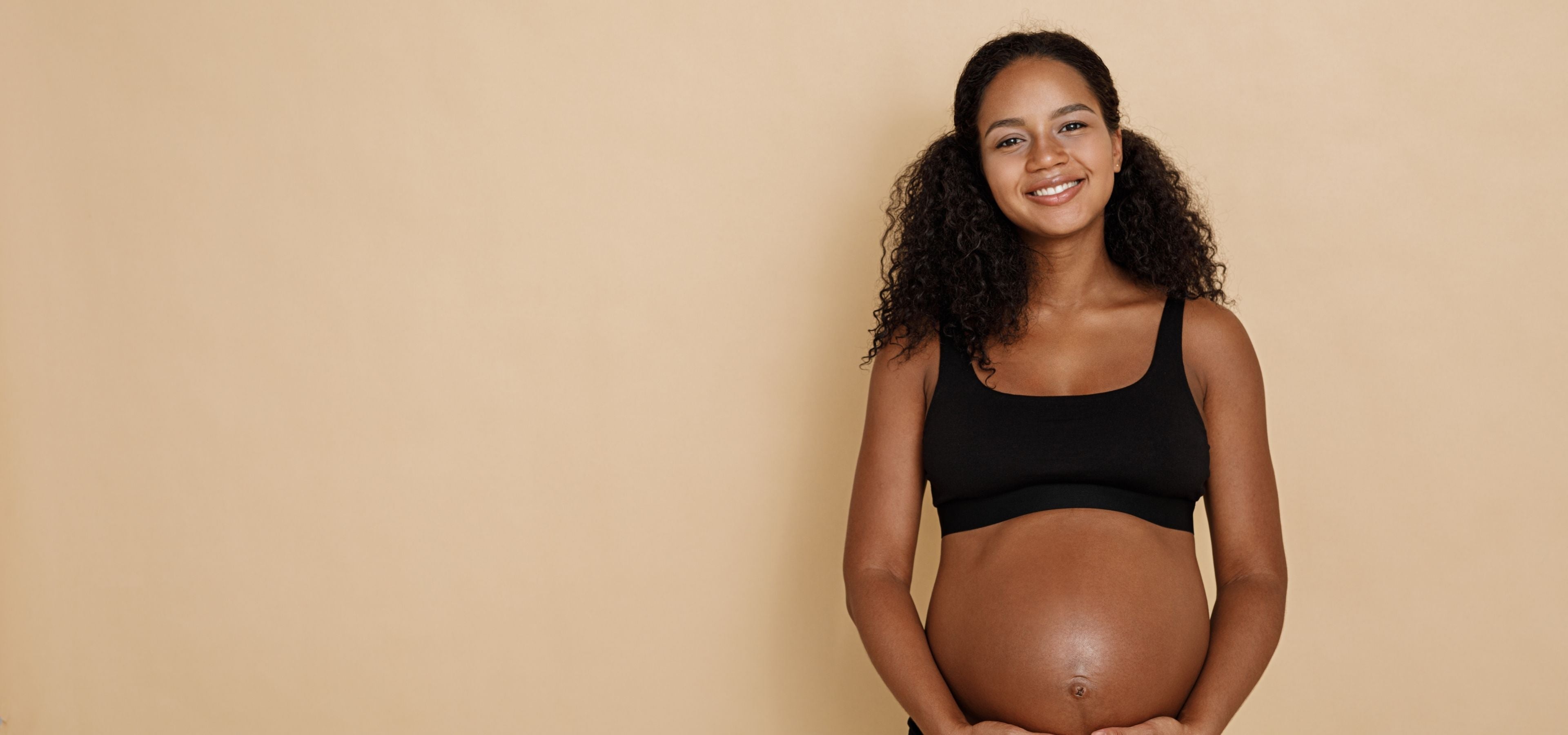Pregnant woman wearing a black tank top against a beige background