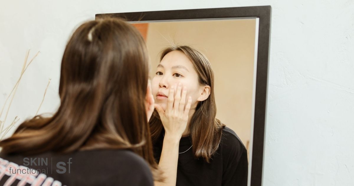 Woman checking her skin in the mirror, assessing her complexion for signs of repair and recovery